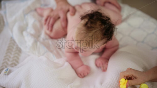 Woman trying to distract a crying baby lying on a blanket during massage with a toy