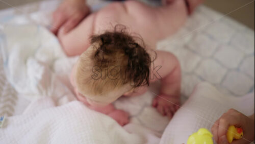 Woman trying to distract a crying baby lying on a blanket during massage with a toy