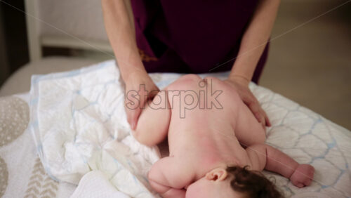 Baby lying on their tummy while an adult massages them and performs mobility exercises
