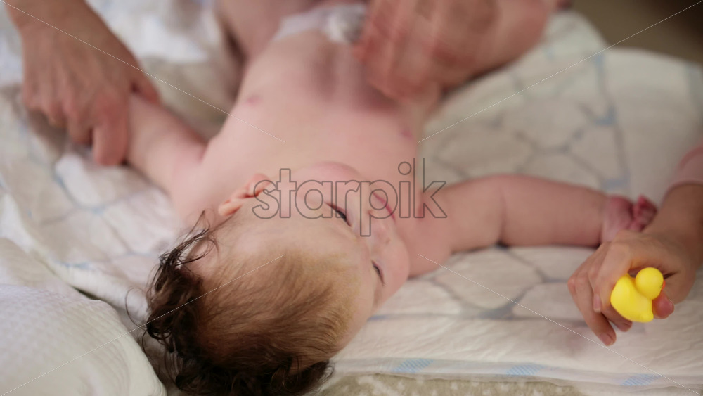 Woman trying to distract a crying baby lying on a blanket during massage with a toy
