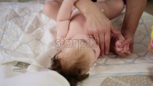 Woman trying to distract a crying baby lying on a blanket during massage with a toy