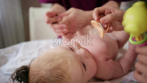 Woman trying to distract a crying baby lying on a blanket during massage with a toy
