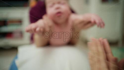 Baby placed on tummy on a stability ball while adults support the infant's torso and shoulders