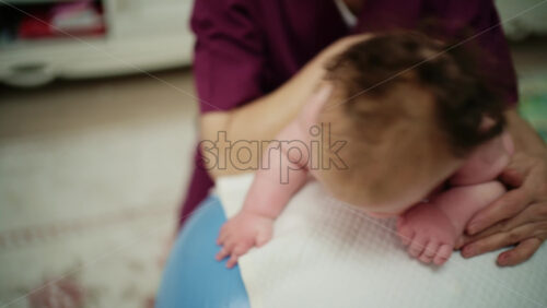 Baby placed on tummy on a stability ball while adults support the infant's torso and shoulders