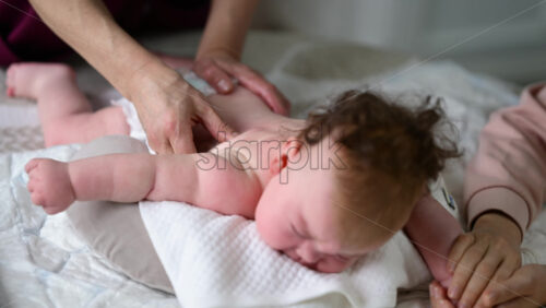 Baby lying on their tummy while an adult massages them and performs mobility exercises