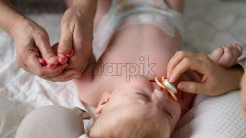 Baby lying on their back while an adult massages them and the mother holds the pacifier in the baby's mouth