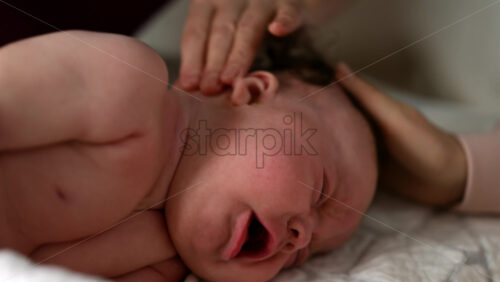 Woman trying to distract a crying baby lying on a blanket during massage with a toy