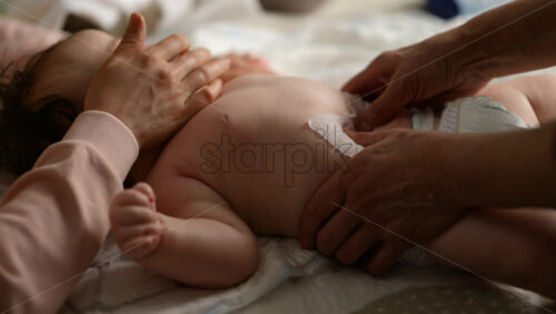 Baby lying on their back while an adult massages them and the mother holds the pacifier in the baby's mouth
