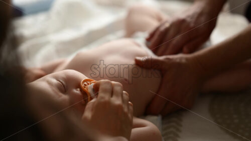 Baby lying on their back while an adult massages them and the mother holds the pacifier in the baby's mouth