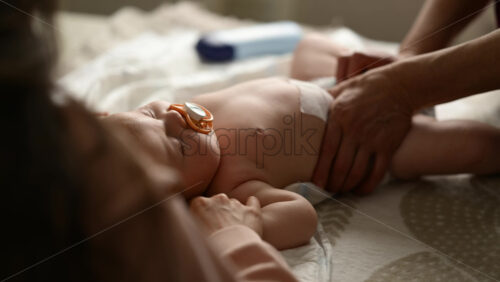 Baby lying on their back while an adult massages them and the mother gently holds the baby's hand