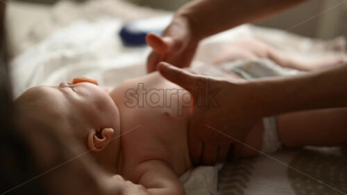 Baby lying on their back while an adult massages them and the mother gently holds the baby's hand