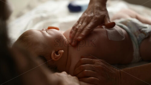 Baby lying on their back while an adult massages them and the mother gently holds the baby's hand