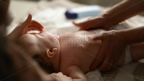 Baby lying on their back while an adult massages them and the mother holds the pacifier in the baby's mouth