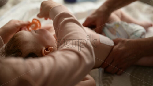 Baby lying on their back while an adult massages them and the mother gently holds the baby's hand