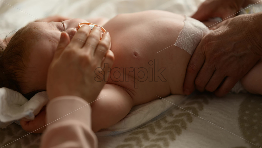 Baby lying on their back while an adult massages them and the mother holds the pacifier in the baby's mouth