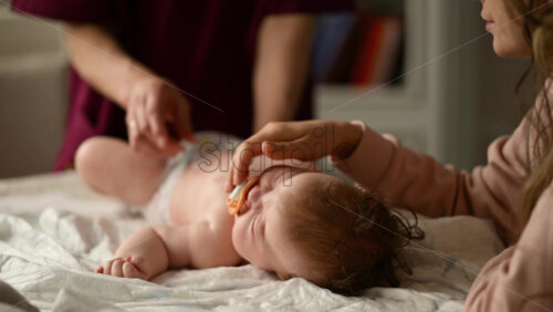 Baby lying on their back while an adult massages them and the mother holds the pacifier in the baby's mouth