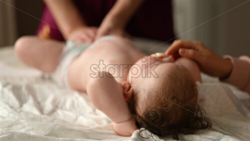 Baby lying on their back while an adult massages them and the mother holds the pacifier in the baby's mouth