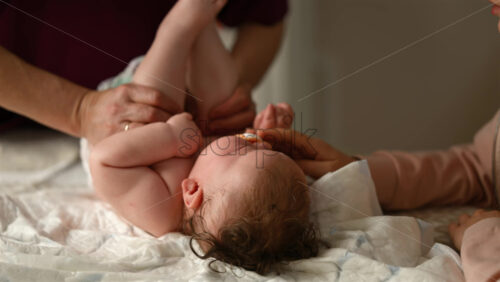 Baby lying on their back while an adult massages them and the mother holds the pacifier in the baby's mouth