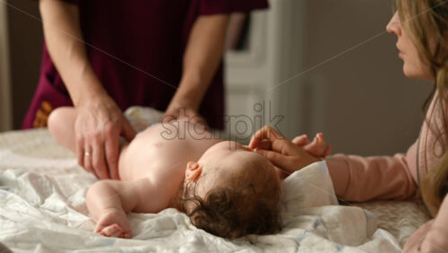 Baby lying on their back while an adult massages them and the mother holds the pacifier in the baby's mouth