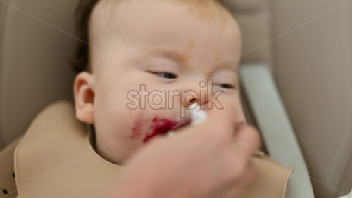 Infant seated in a high chair while an adult feeds the baby with a spoon