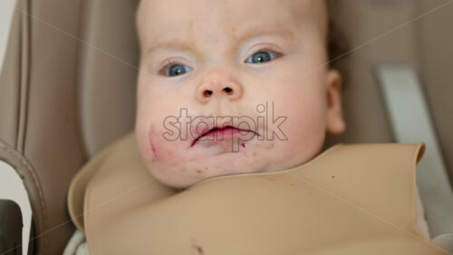 Infant seated in a high chair while an adult feeds the baby with a spoon