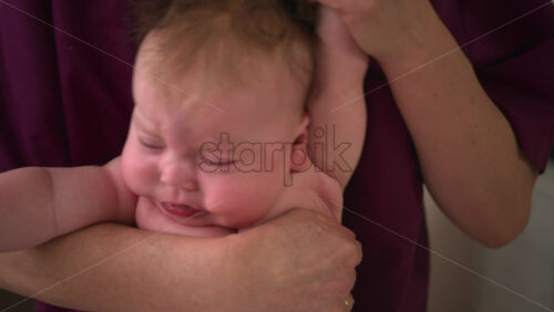 Infant lying face down across a caregiver's forearm, supported securely