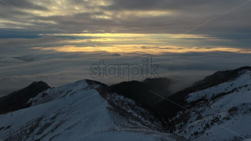 Panoramic aerial drone view of golden sunrise above clouds, winter landscape in the mountains. Transylvania, Mount Ciucas in Romania