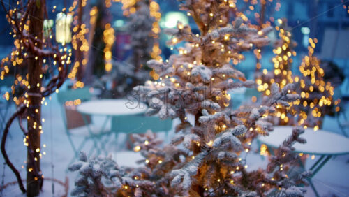 Close up of a small Christmas tree covered in snow and decorated with warm string lights outdoors - Starpik Stock