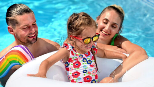 Happy parents and their daughter in rubber ring are swimming in the pool. Slow motion