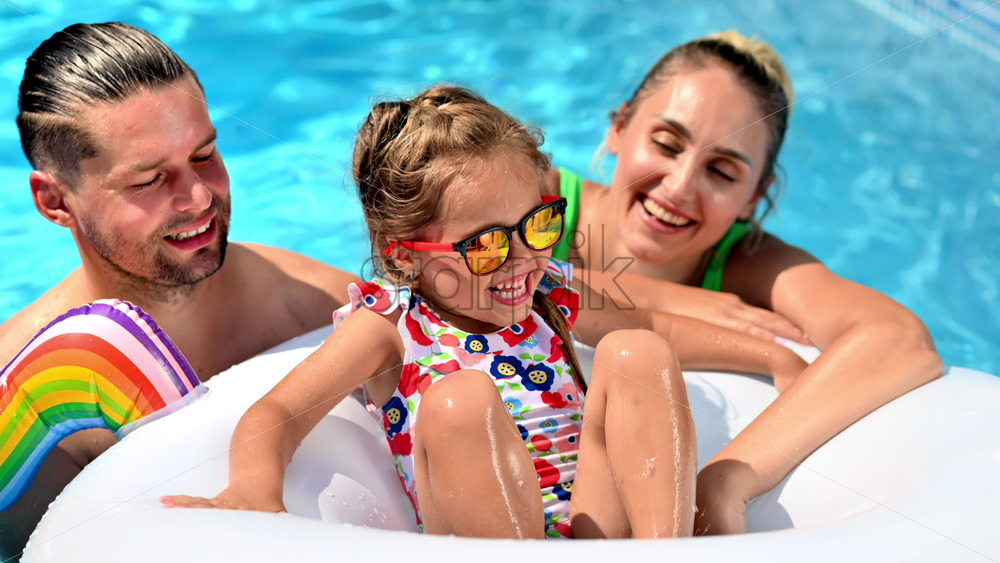 Happy parents and their daughter in rubber ring are swimming in the pool. Slow motion