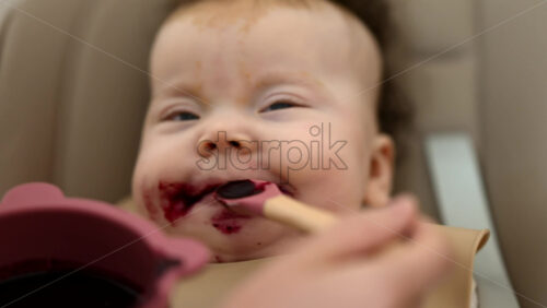 Infant seated in a high chair while an adult feeds the baby with a spoon - Starpik Stock