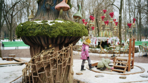 Winter park scene with children playing near a whimsical treehouse style structure decorated with moss and fairy tale elements - Starpik Stock
