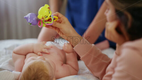 Woman trying to distract a crying baby lying on a blanket during massage with a toy - Starpik Stock