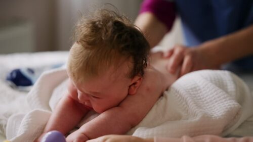 Baby lying on their back while an adult massages them and performs mobility exercises
