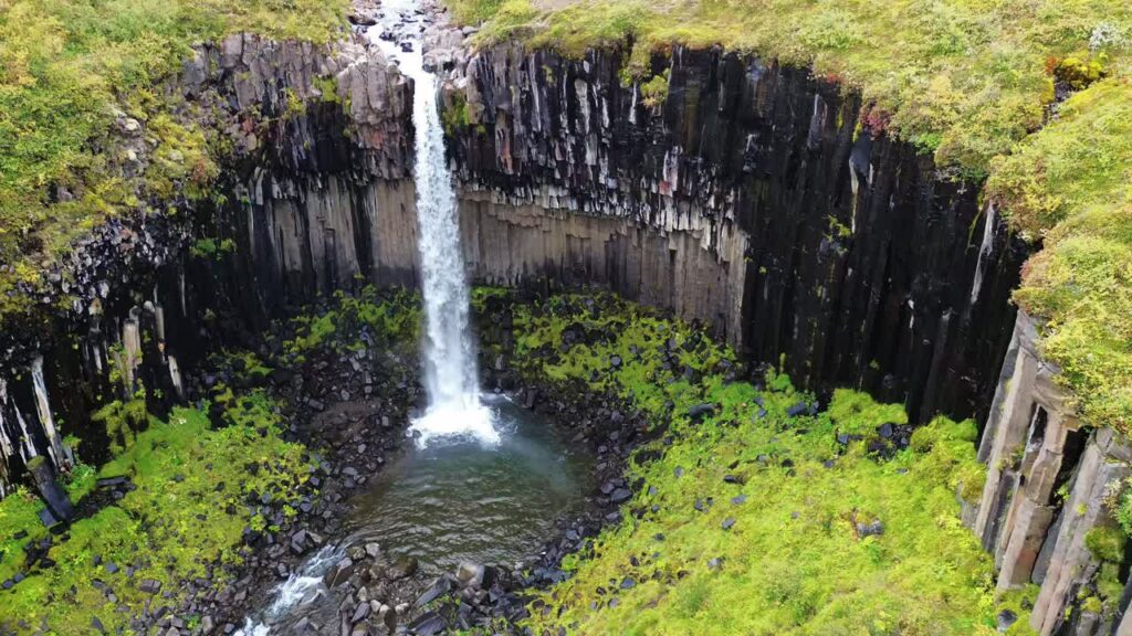 Video – Aerial drone view of Svartifoss waterfall cascading down dramatic basalt column cliffs in Vatnajokull National Park, Iceland - Starpik Stock