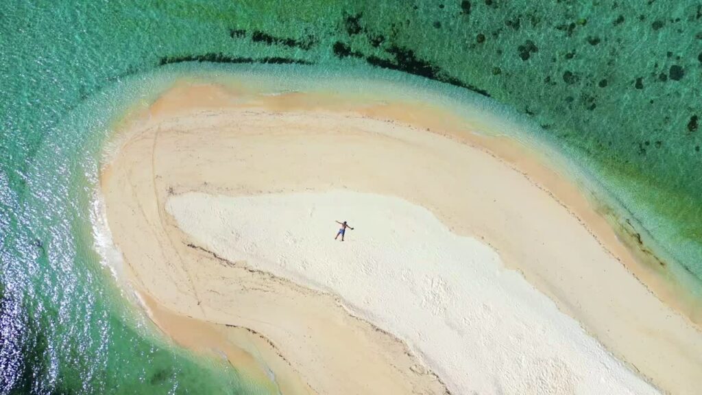 Video – Aerial drone view of a lone traveler standing on the white sandbar of Ditaytayan Island in Culion, Palawan, Philippines. Clear turquoise water surrounds the isolated tropical beach - Starpik Stock