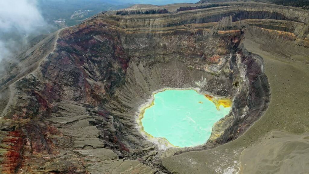 Video – Aerial drone view of a turquoise crater lake inside a volcanic crater in Guatemala, surrounded by rugged volcanic rock formations and geothermal landscape - Starpik Stock