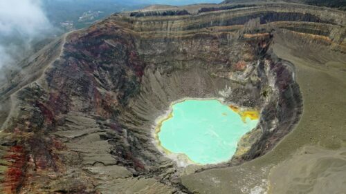 Video – Aerial drone view of a turquoise crater lake inside a volcanic crater in Guatemala, surrounded by rugged volcanic rock formations and geothermal landscape - Starpik Stock