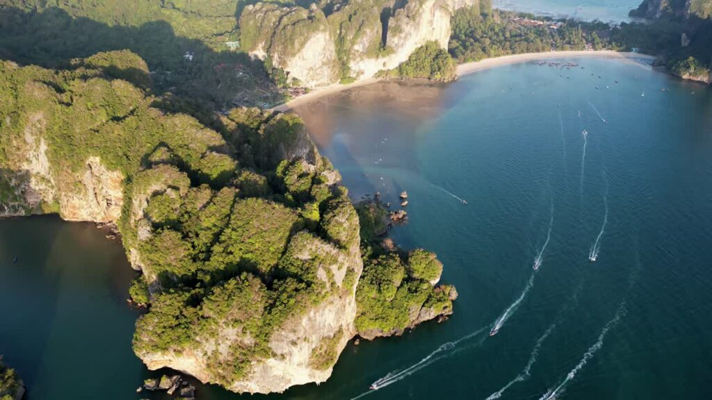Video – Aerial drone view of boats moving across turquoise water near dramatic limestone cliffs and beach in Krabi, Thailand - Starpik Stock