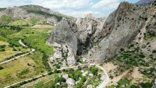 Video – Aerial drone view of rocky mountains and canyon landscapes with a small stone bridge crossing a river below, surrounded by rugged terrain and green valley vegetation - Starpik Stock