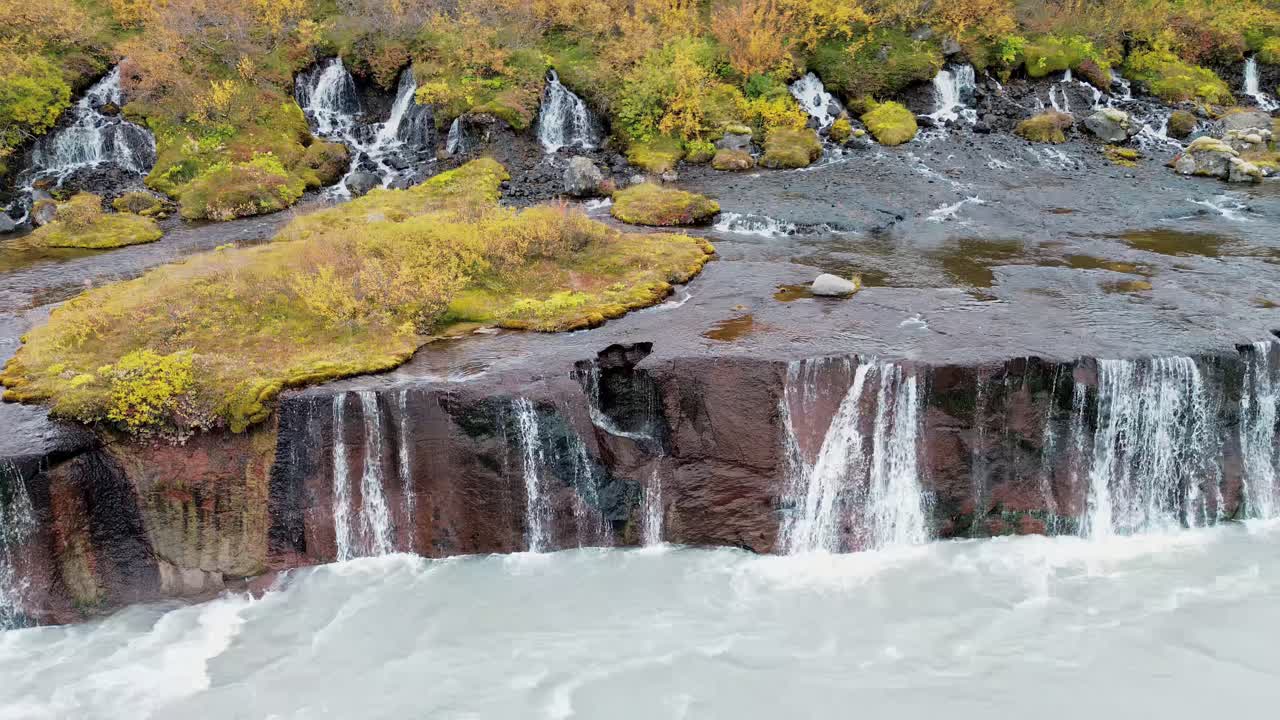 Video – Aerial drone view of the Hraunfossar waterfalls, where dozens of small streams emerge from lava fields and cascade into the Hvita river. Moss covered rocks and autumn vegetation frame the unique series of waterfalls in western Iceland - Starpik Stock