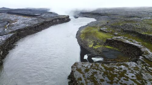 Video – Aerial drone view of the Jokulsa a Fjollum river winding through a barren volcanic plateau near Dettifoss. Moss covered rocks and dark lava formations frame the powerful glacial river - Starpik Stock