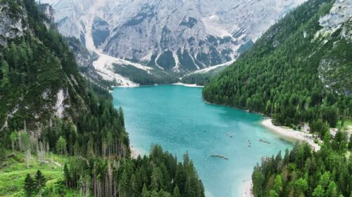 Video – Aerial drone view of the turquoise waters of Lago di Braies surrounded by dense alpine forest and dramatic limestone mountains in the Dolomites, Italy - Starpik Stock