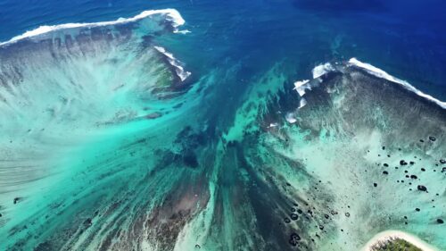 Video – Aerial drone view of turquoise lagoon waters and coral reef formations in Mauritius, with waves breaking along the reef line in the Indian Ocean - Starpik Stock