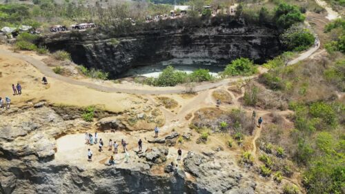 Video - Aerial drone view of Broken Beach in Nusa Penida, Bali, Indonesia. Turquoise ocean water flows through the natural rock arch into a secluded circular cove surrounded by dramatic limestone cliffs