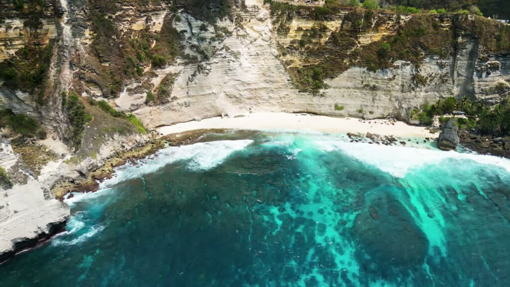 Video - Aerial drone view of Diamond Beach and its iconic offshore rock pinnacle in Nusa Penida, Bali. Powerful ocean waves meet dramatic limestone cliffs and lush tropical vegetation