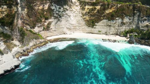 Video - Aerial drone view of Diamond Beach and its iconic offshore rock pinnacle in Nusa Penida, Bali. Powerful ocean waves meet dramatic limestone cliffs and lush tropical vegetation