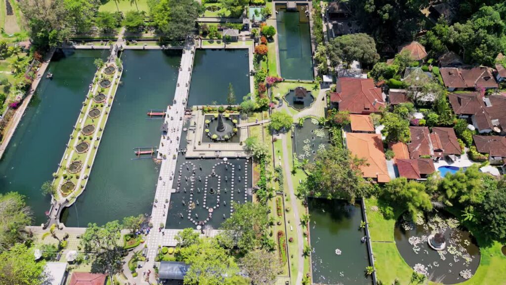 Video - Aerial drone view of Tirta Gangga Water Palace in Karangasem, East Bali, Indonesia. Symmetrical royal gardens with ornamental ponds, fountains, stepping stones, and traditional Balinese architecture surrounded by lush greenery