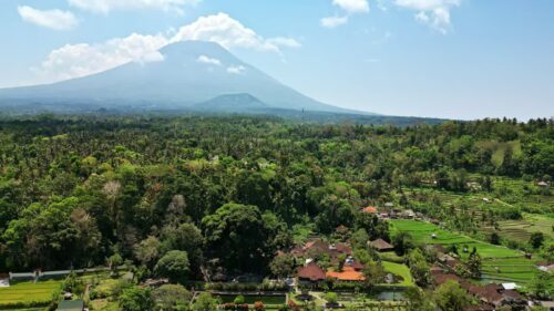 Video - Aerial drone view of Mount Agung volcano rising above palm forests and rice fields in East Bali, Indonesia. Hazy tropical atmosphere with traditional Balinese villages in the foreground