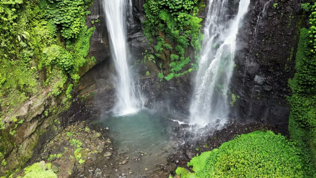 Video - Aerial drone view of twin waterfalls cascading down a steep jungle cliff at Sekumpul Waterfall, Buleleng, Bali. White water streams contrast with deep green rainforest vegetation